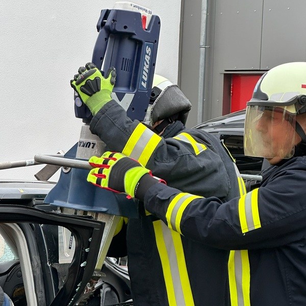 Zwei Feuerwehrleute in Schutzkleidung und Helmen bedienen hydraulisches Rettungsgerät an einem demolierten Auto. PKW Unfallrettung Seminar