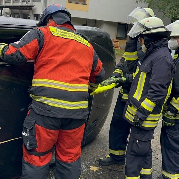 Einsatzkräfte in Schutzkleidung führen Unfallrettungstraining an einem seitlich liegenden Fahrzeug durch. PKW Unfallrettung Seminar