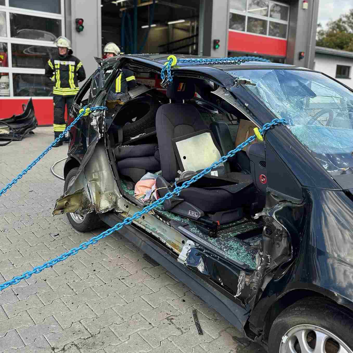 Beschädigtes schwarzes Auto mit zerbrochenem Fenster und blauen Ketten, die zur Stabilisierung durch Feuerwehrleute verwendet werden. Kettenrettung nach der Oslomethode - Training Technical Resuce RH