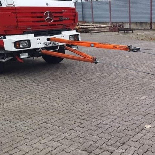 Roter Mercedes-LKW mit angehängter oranger Seilwinde und Zugvorrichtung auf einem gepflasterten Hof. Maschinelle Zugeinrichtung Seminar