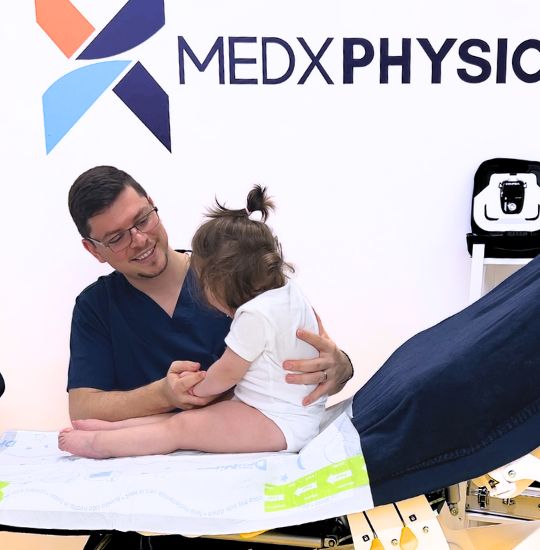 Image of a physio staff helping a little boy to do some physical exercises for legs with a rubber band