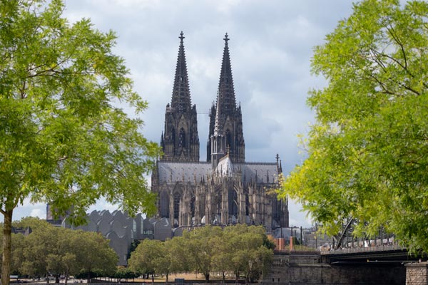 Kölner Dom von Bäumen umrahmt an einem wolkigen Tag