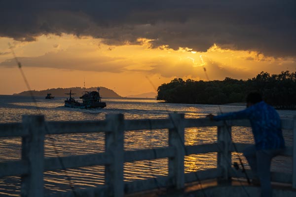 Fischerboot unterwegs im Abendlicht vor Mangroven