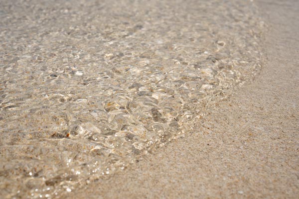 Sonnenlicht auf flachem Wasser über feinem Strandsand