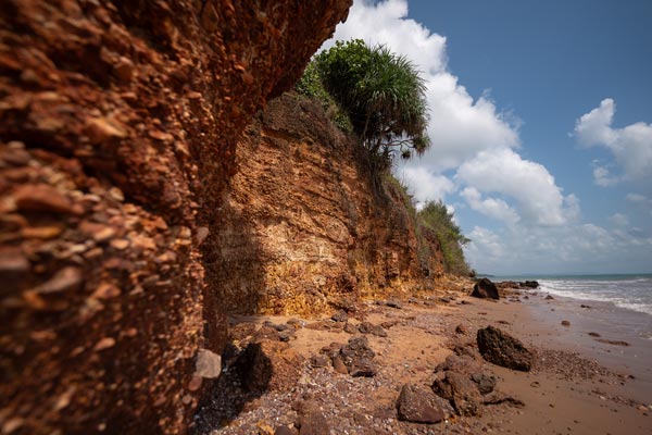 Eroded red sea cliff beside tropical beach