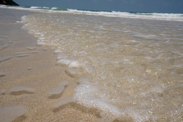 Schaumige Meereswelle am flachen Sandstrand