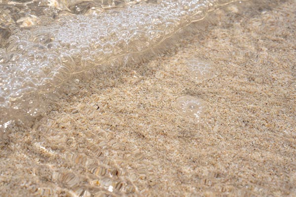 Schaumblasen über geriffeltem Sand im seichten Meer