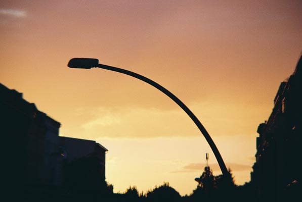 Gebogene Straßenlaterne vor leuchtendem Abendhimmel