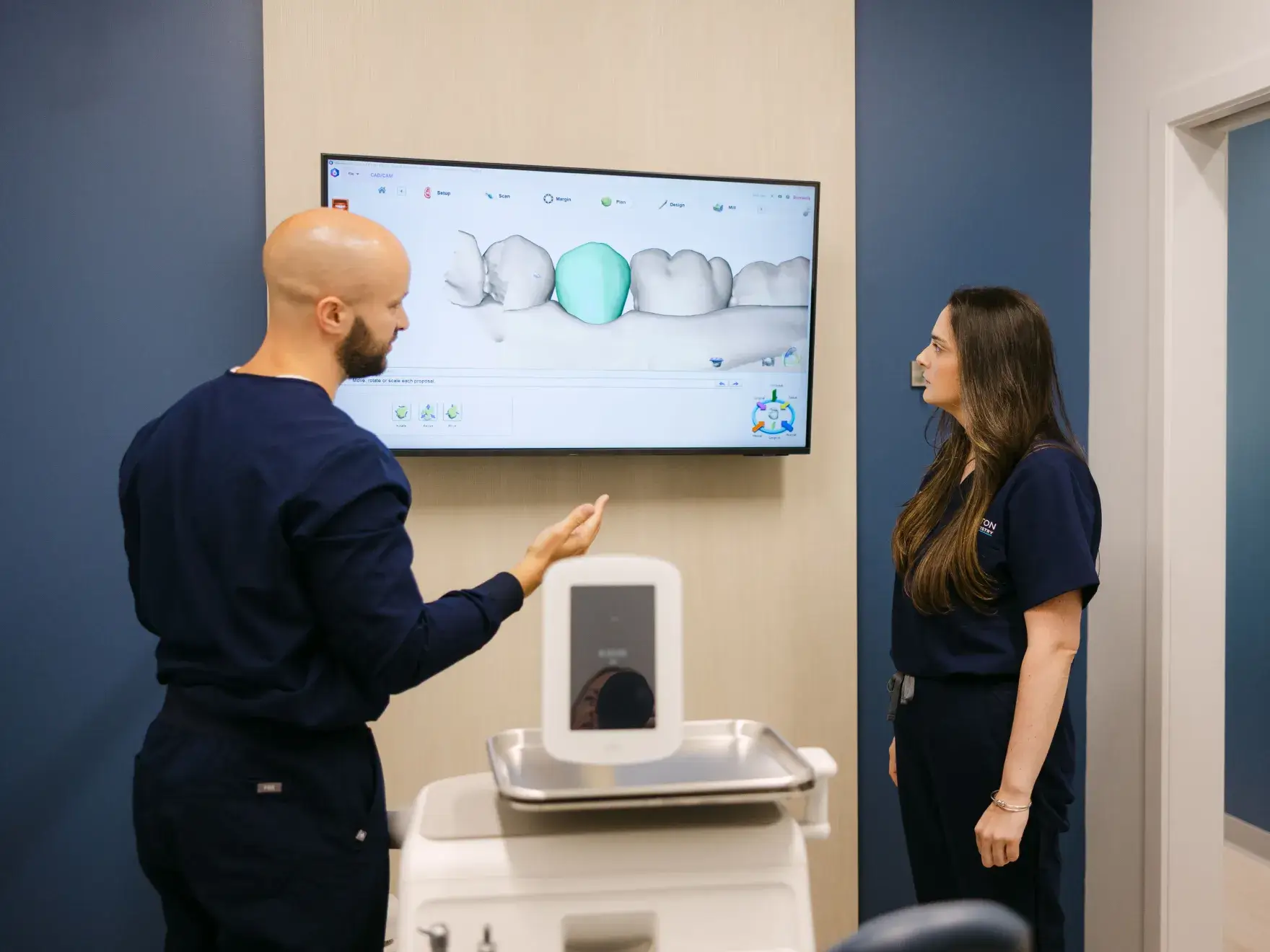 A man and a woman look at a dental scan on a monitor in an office.