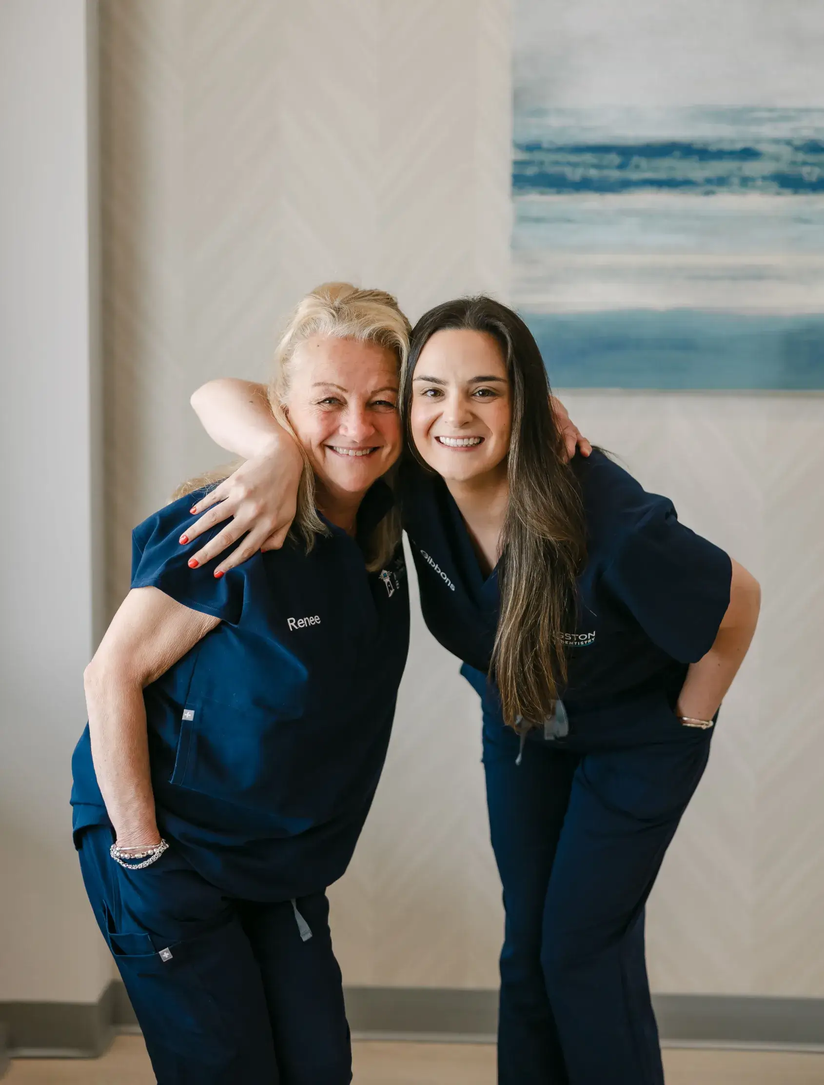 Two women in matching uniforms, smiling and posing together, one with her arm around the other.