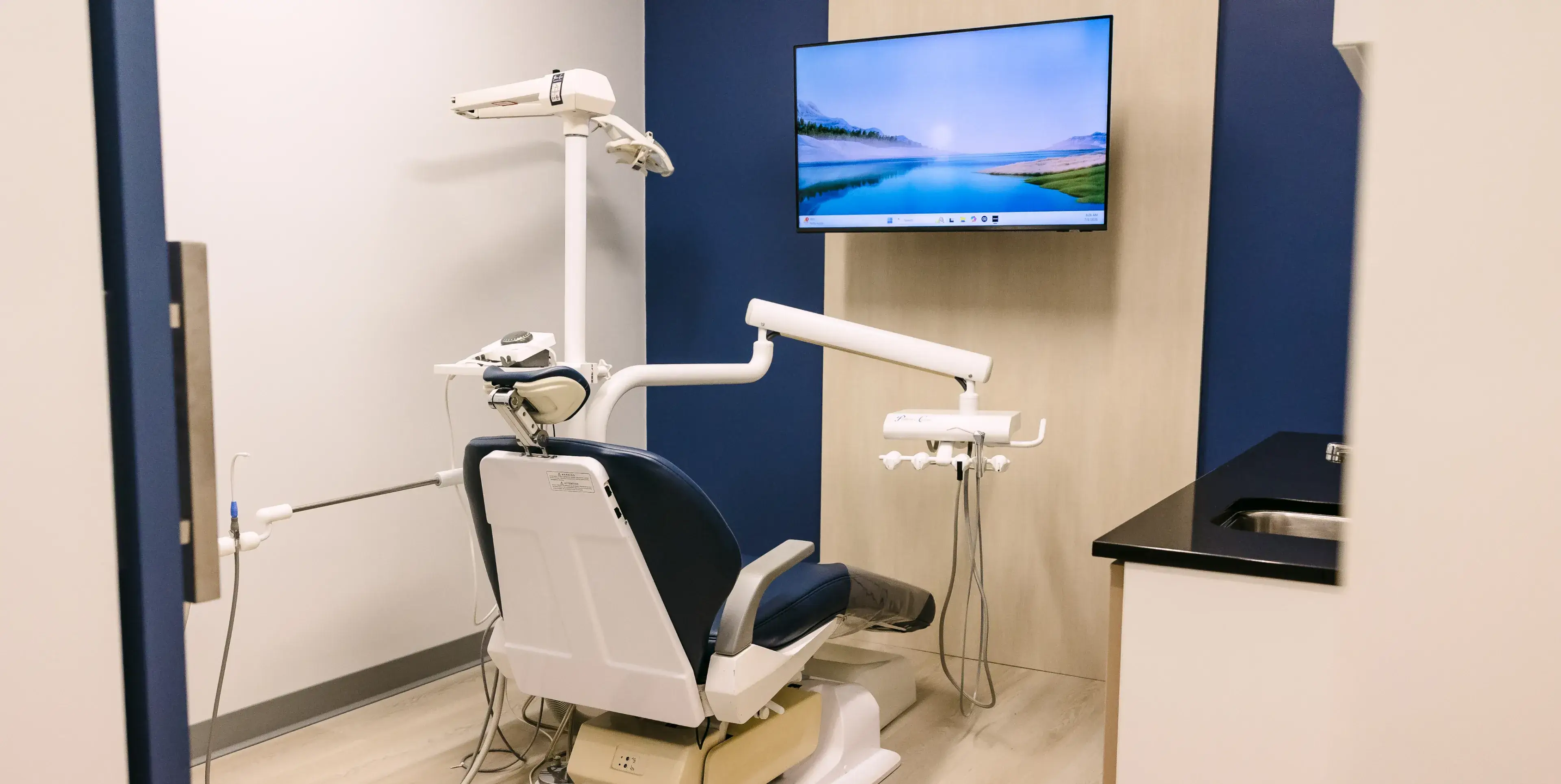 Dental examination room with a chair, dental tools, and a wall-mounted TV showing a landscape.