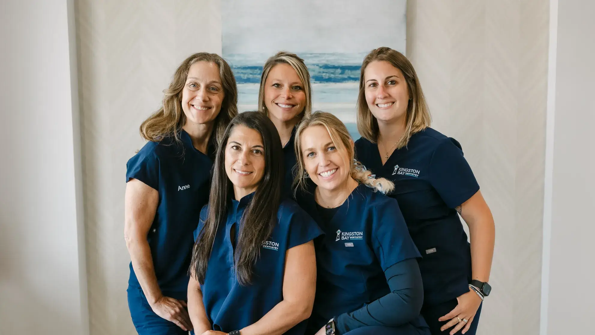 Five women in matching blue uniforms smiling and standing together indoors.
