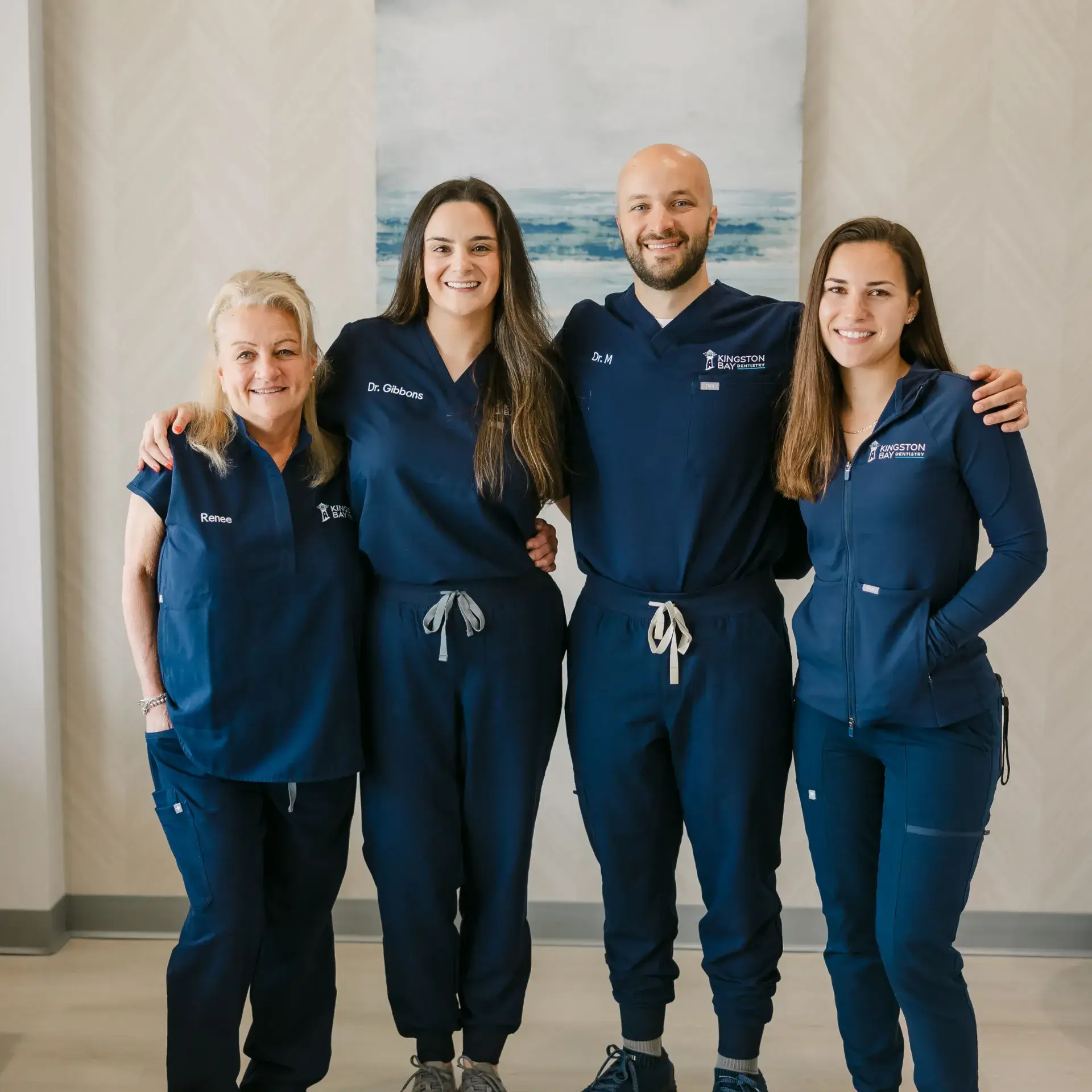 Four people in matching blue uniforms stand together, smiling in a room.