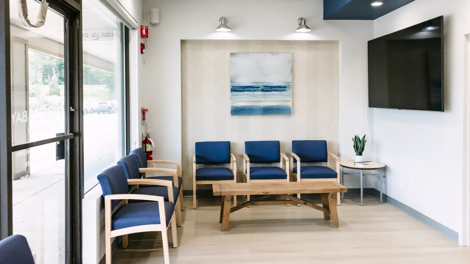 Five blue chairs and a wooden table arranged in a small, clean waiting room.