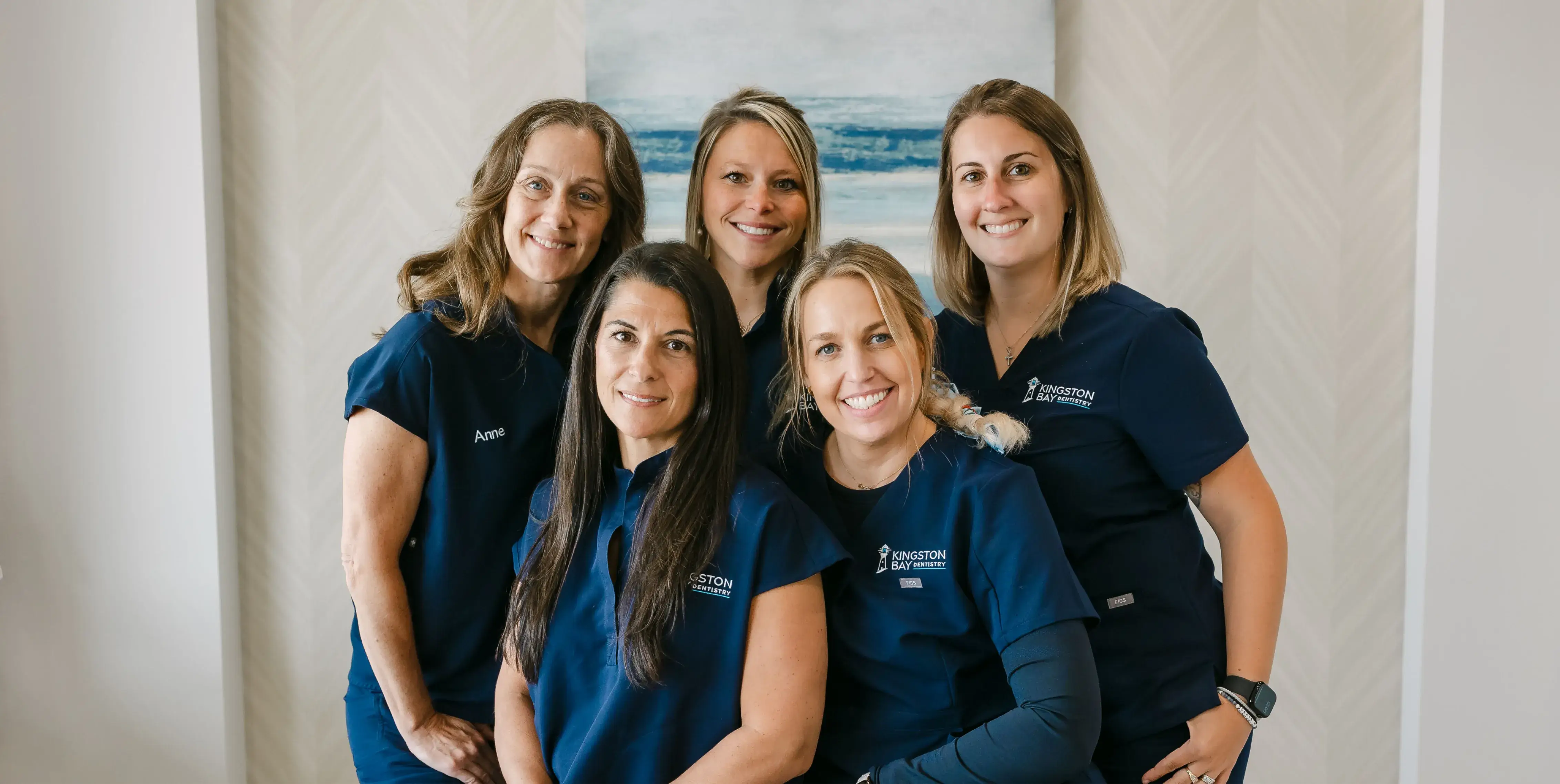 Five women wearing blue uniforms smile while posing for a group photo indoors.