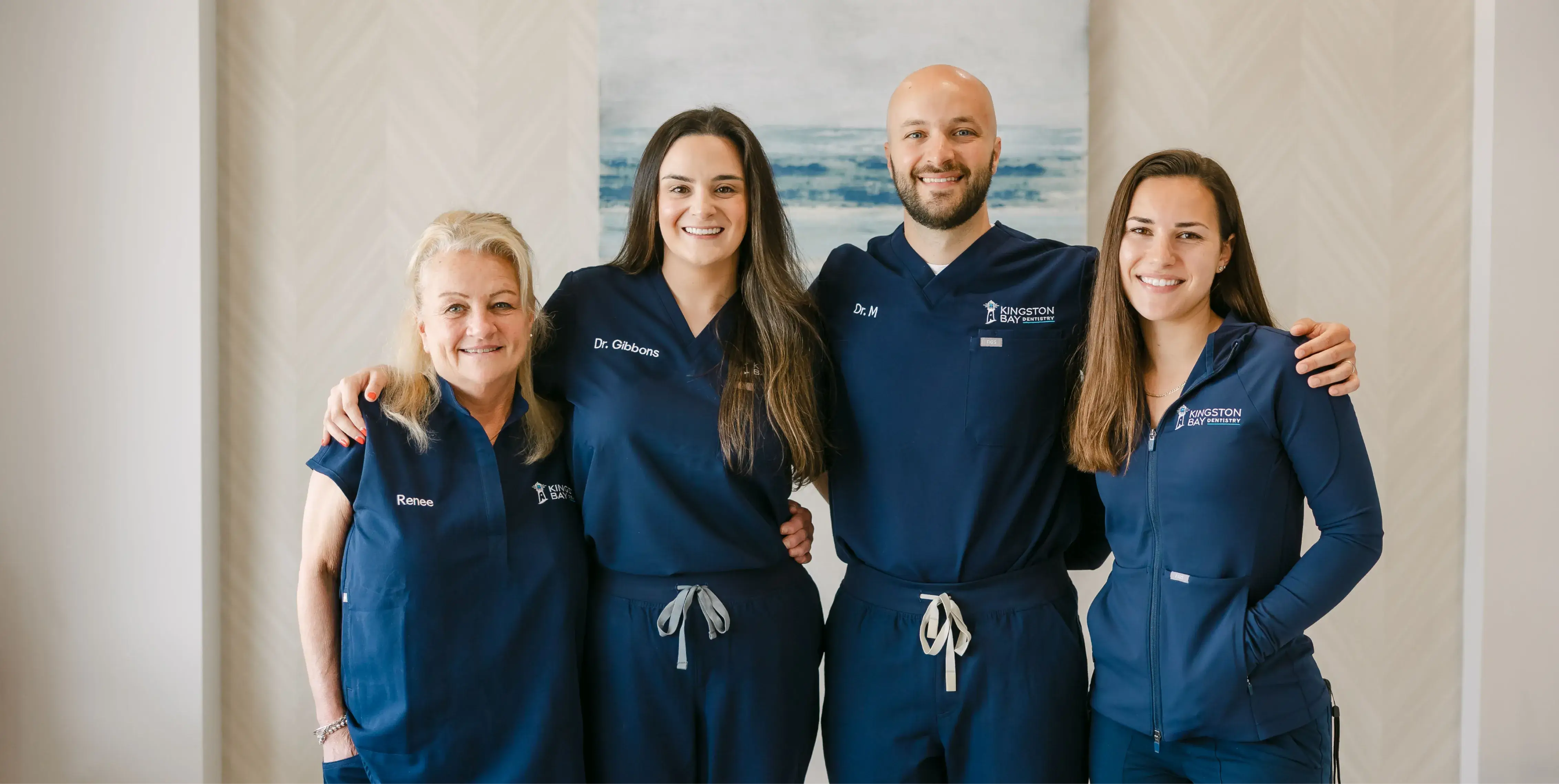 Four people in matching blue outfits smiling and standing close together, arms around each other.