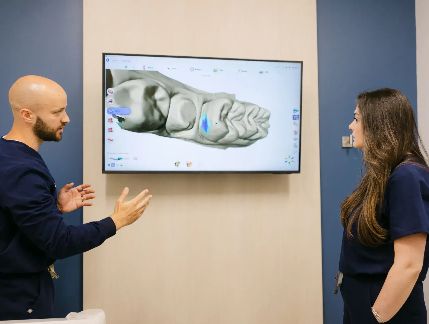 Two people in medical uniforms discuss a 3D model of a foot displayed on a screen.