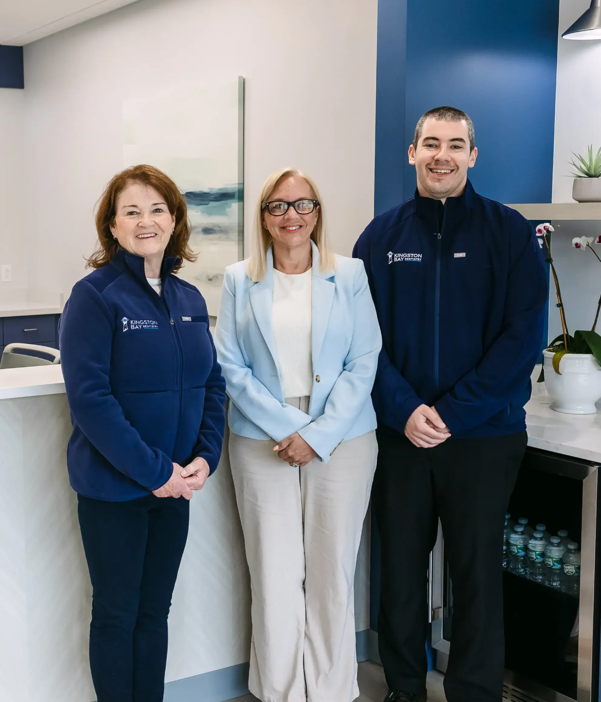 Three people standing together in an office, smiling at the camera.