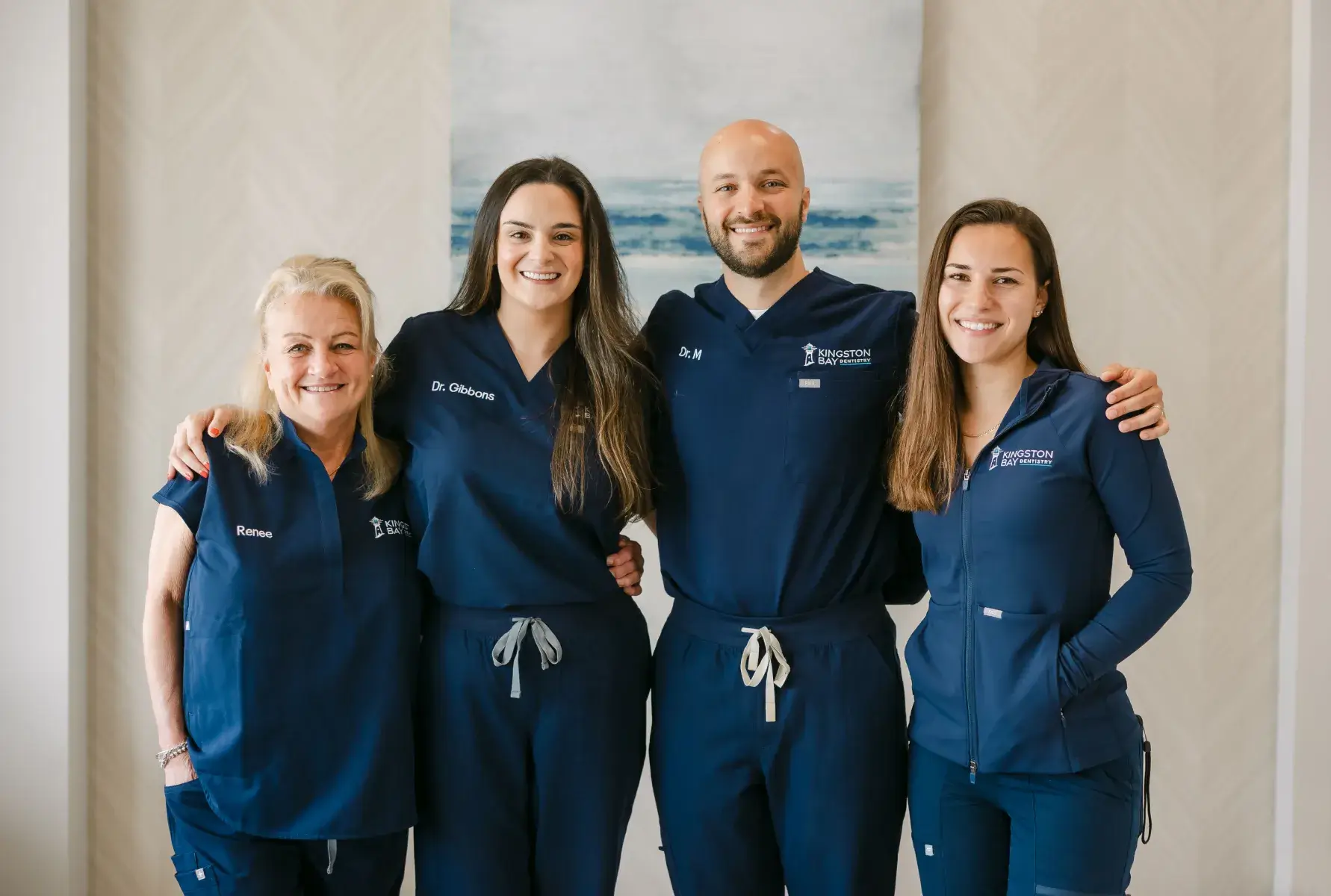 Four people in matching blue uniforms stand smiling indoors, arm in arm.
