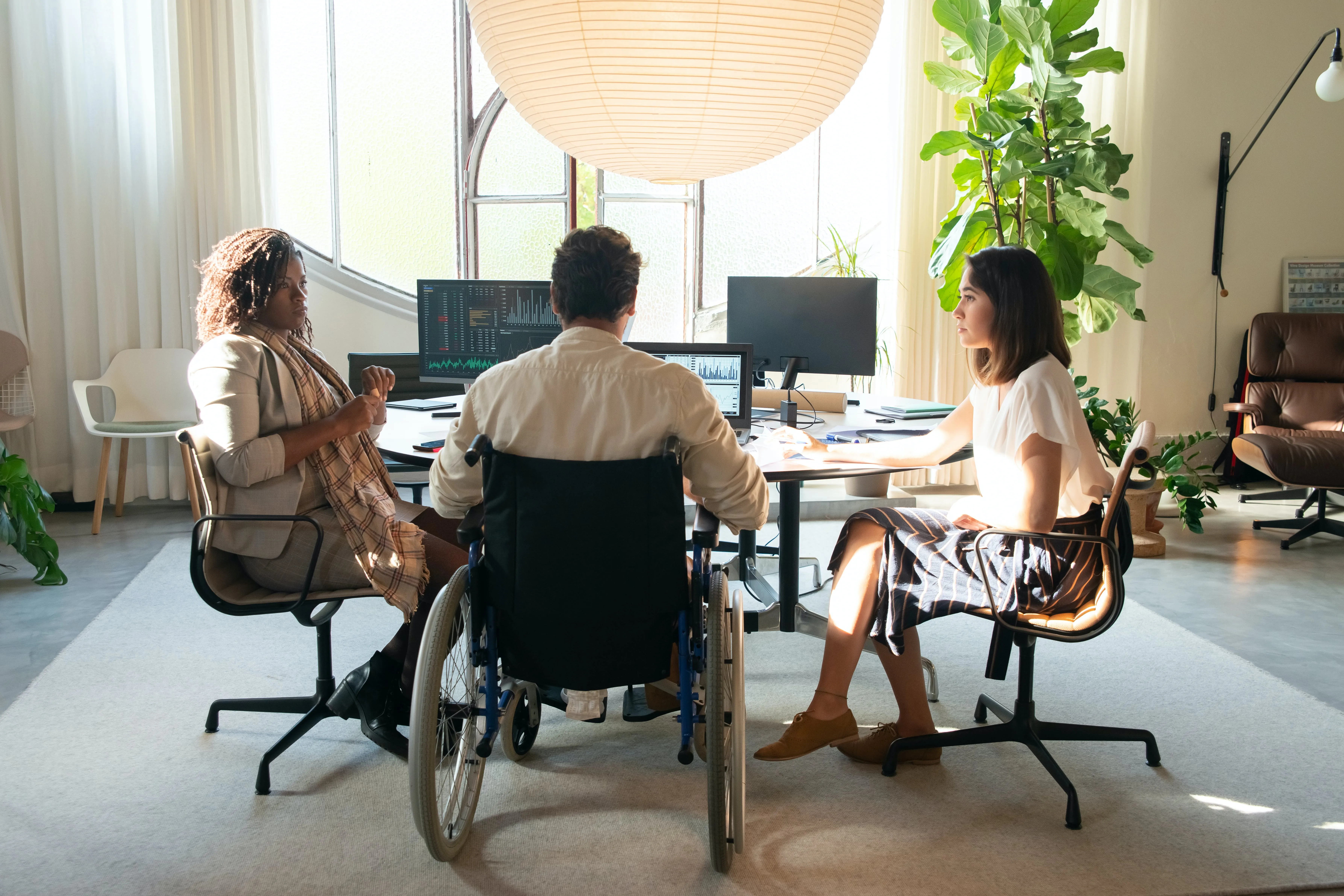 Three people sat around an office table having a meeting, one of them is a wheelchair user