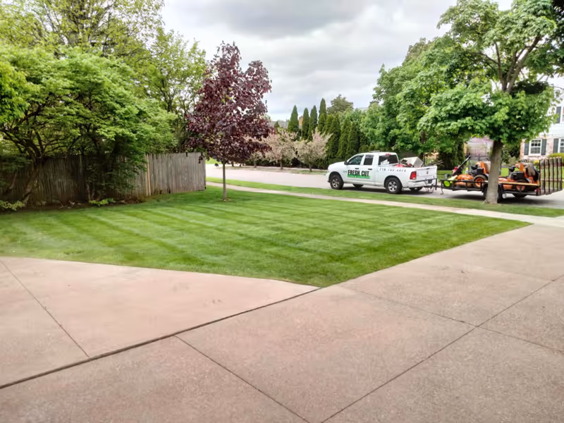 Cleanly edged lawn with defined stripes and a Fresh Cut Lawn & Landscape truck and trailer visible in the background.
