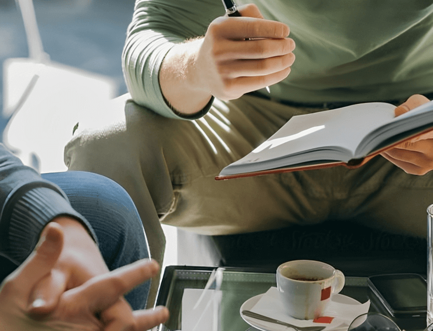 A person sitting at a table with a book and a cup of coffee.