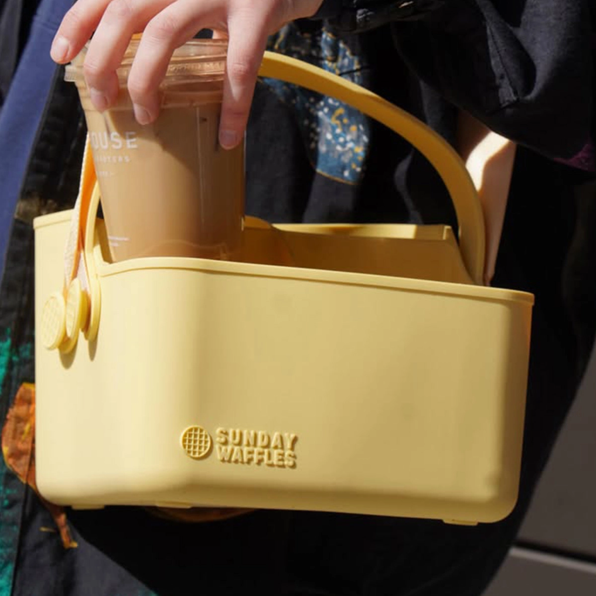 Bevvy Tote in Butter colorway carried by hand, shown with an iced coffee drink