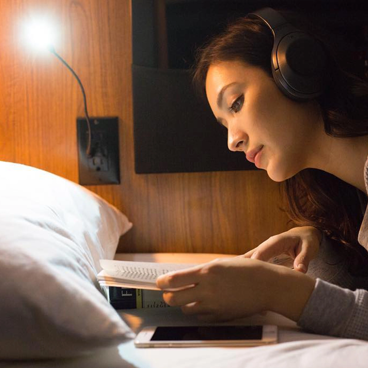 Passenger reading in a Cabin bunk with the reading lamp on, wood panel and soft textiles