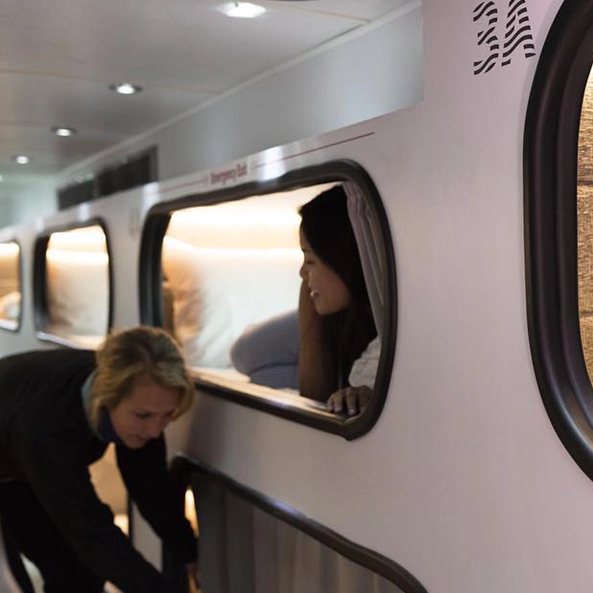 Cabin attendant crouched at a pod opening, talking with a passenger