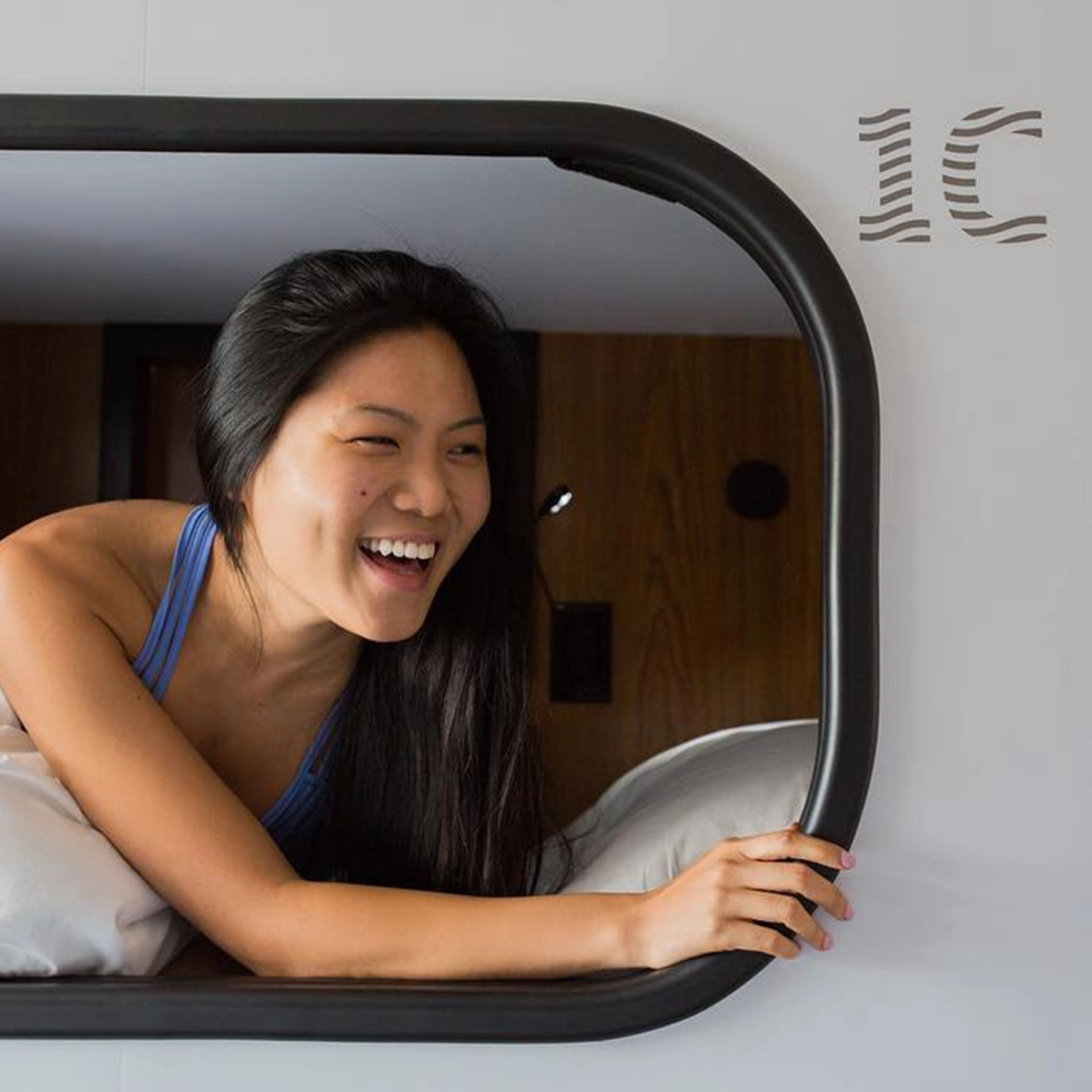 Passenger leaning out of her Cabin sleeping pod, rounded opening and white bedding