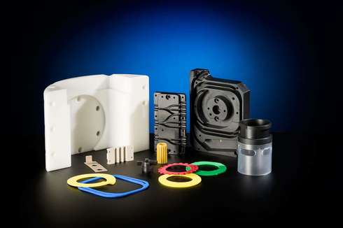 Various plastic and metal mechanical parts including white and black housing pieces, colorful gaskets, and small components arranged on a black surface with a blue gradient background.