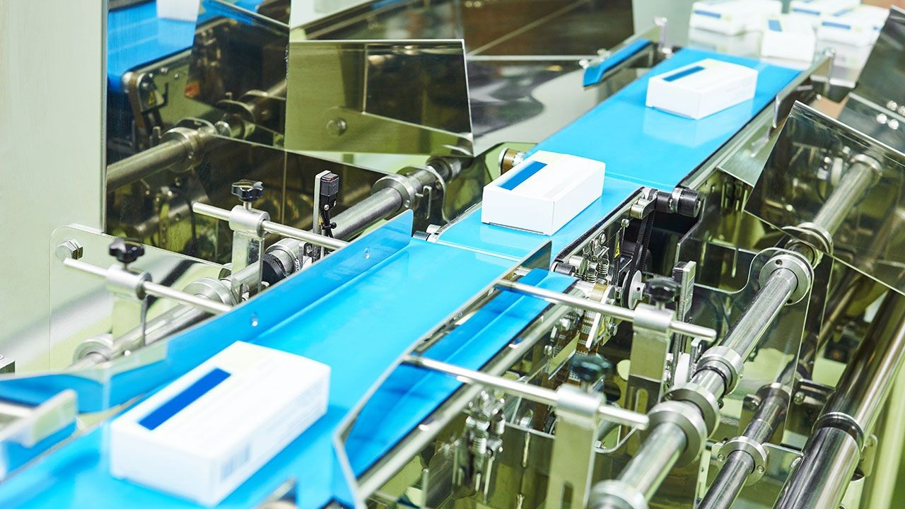 High-speed packaging machine conveyor belt transporting white rectangular boxes.