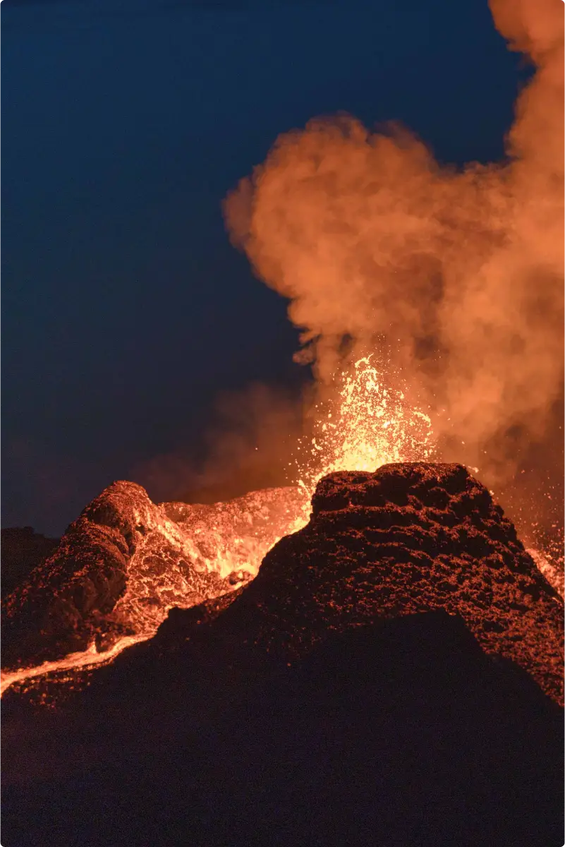 Volcanic eruption at night with lava flows, smoke, and intense flames under sky.