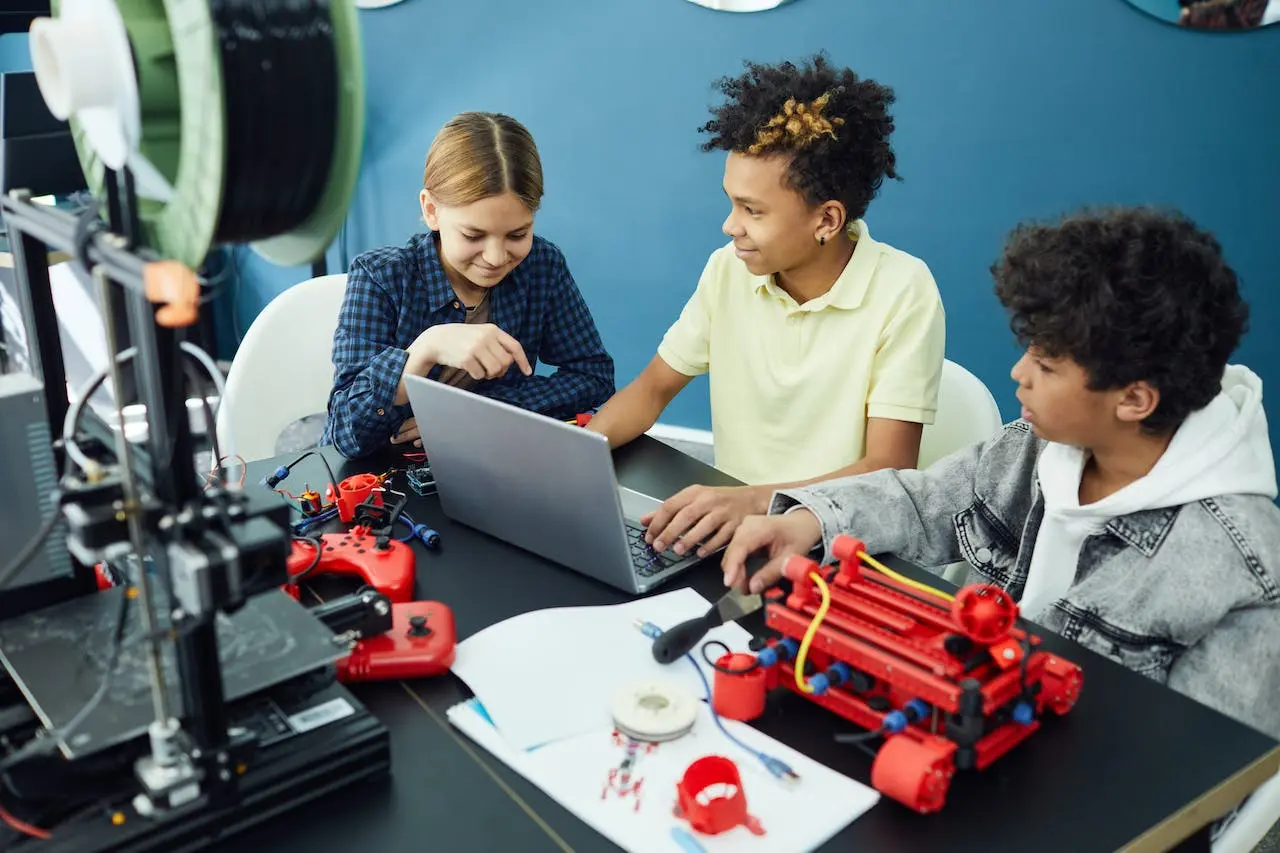 Middle school students working on a 3D printing and robotics project with laptop and tools in a STEM classroom.