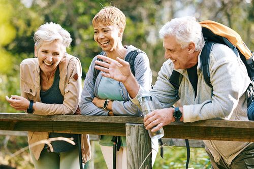 Three retirees, two women and one man, leaning on a wooden beam outdoors. Chatting and laughing .