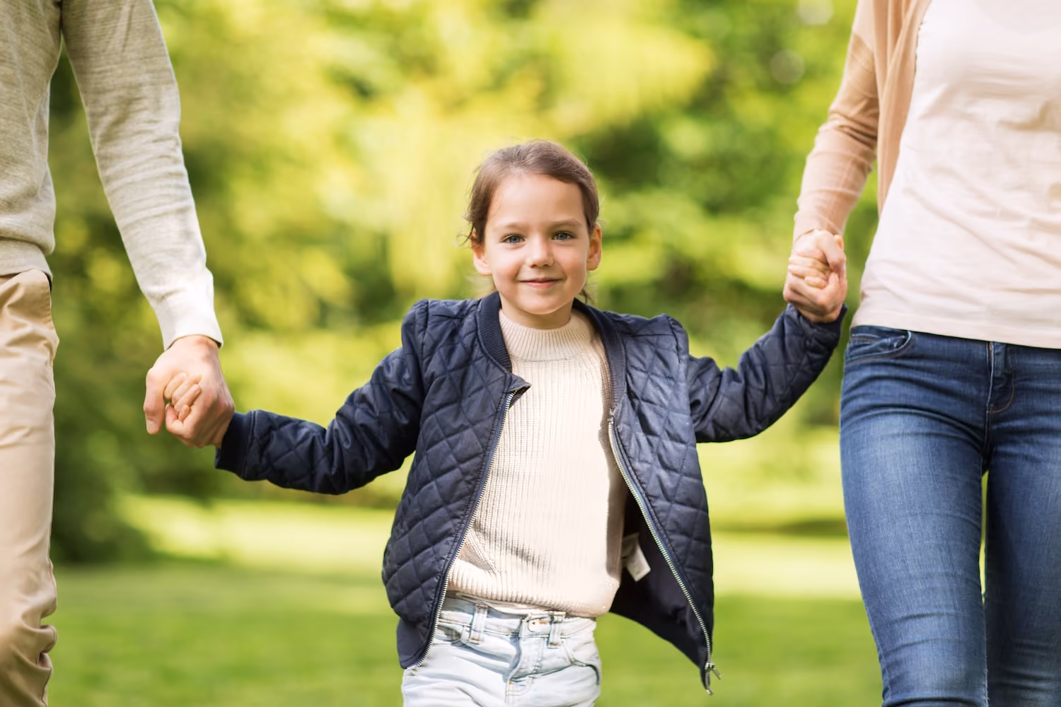 child walking through park holding hands with two adults