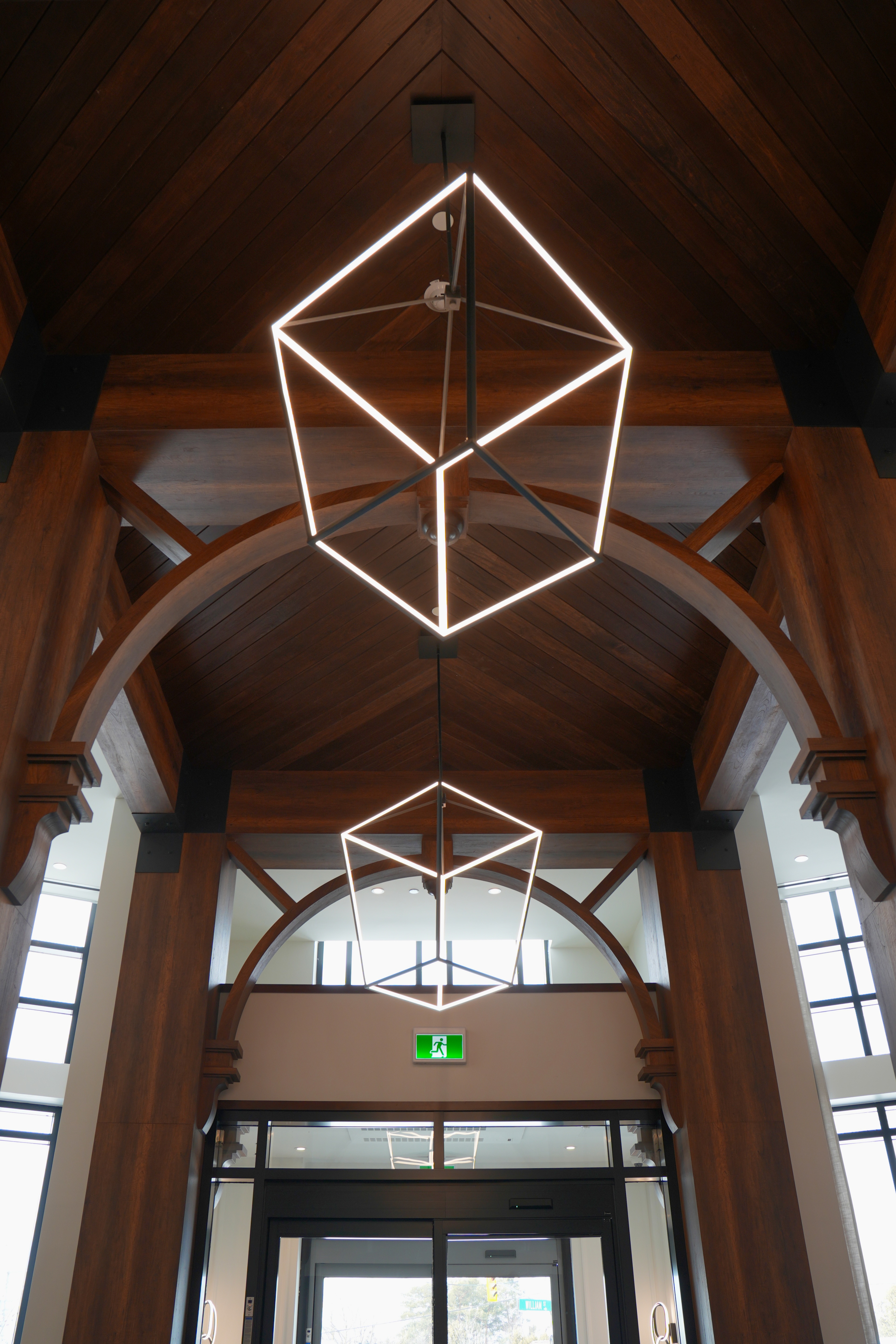 Interior entrance with modern geometric pendant lights and dark wooden ceiling beams framing a glass doorway.