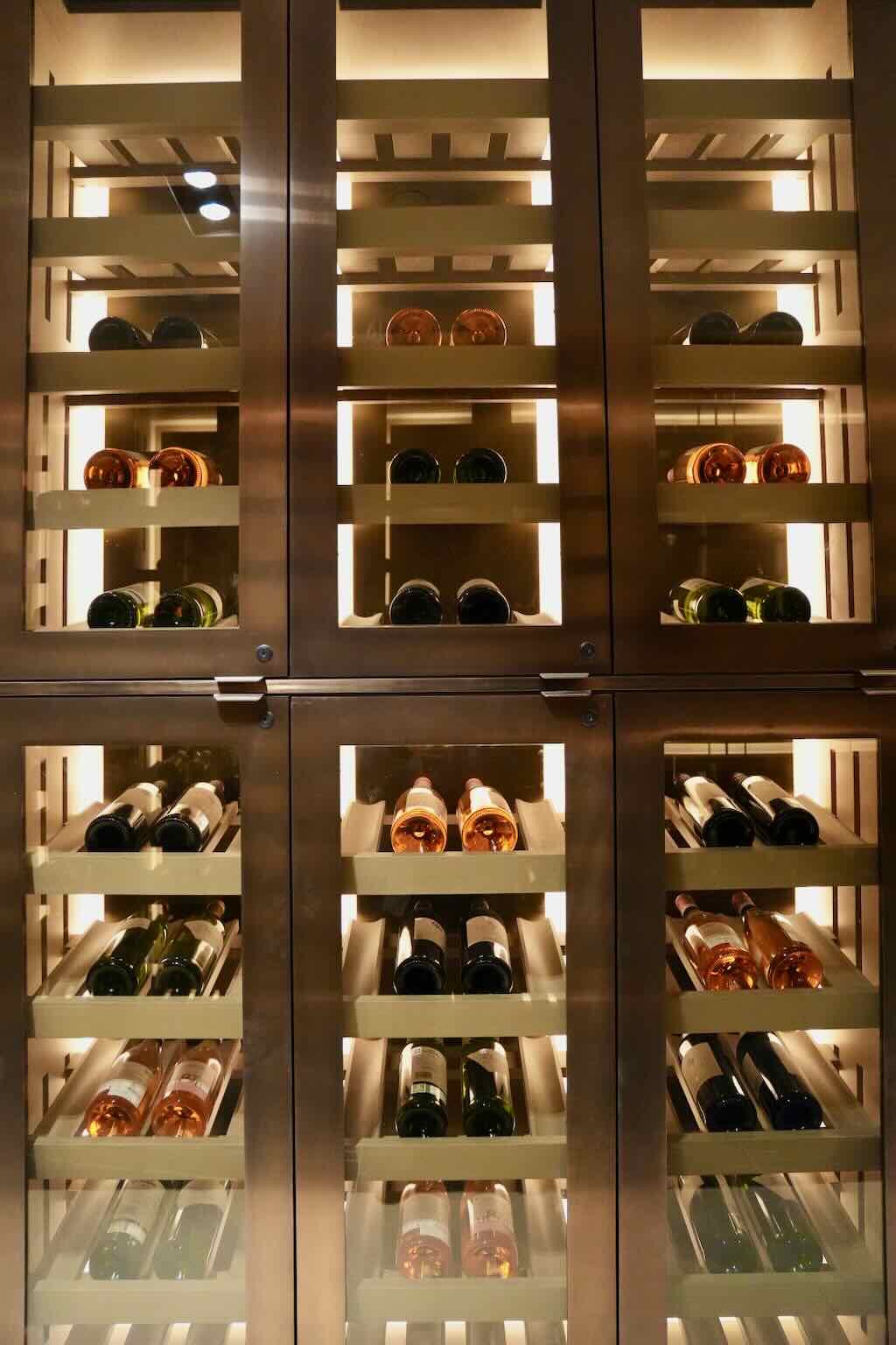 Lit wine refrigerator with multiple bottles of white, rosé, and red wine stored on horizontal racks behind glass doors.