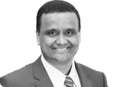 Riaz smiling at camera, headshot photo in black and white, wearing a suite and tie