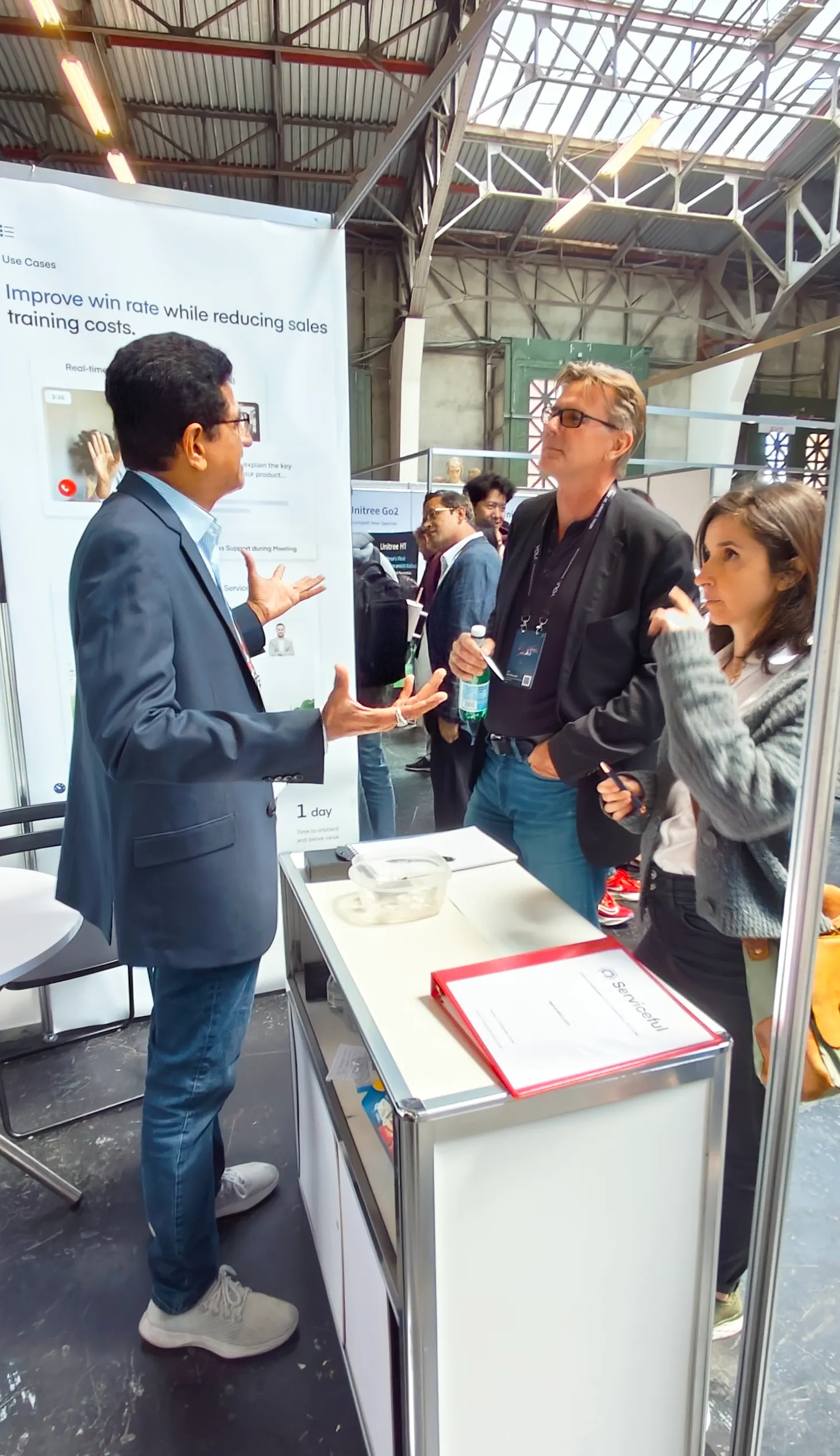 A Serviceful team member presenting the sales enablement platform to two attendees at the company's expo booth