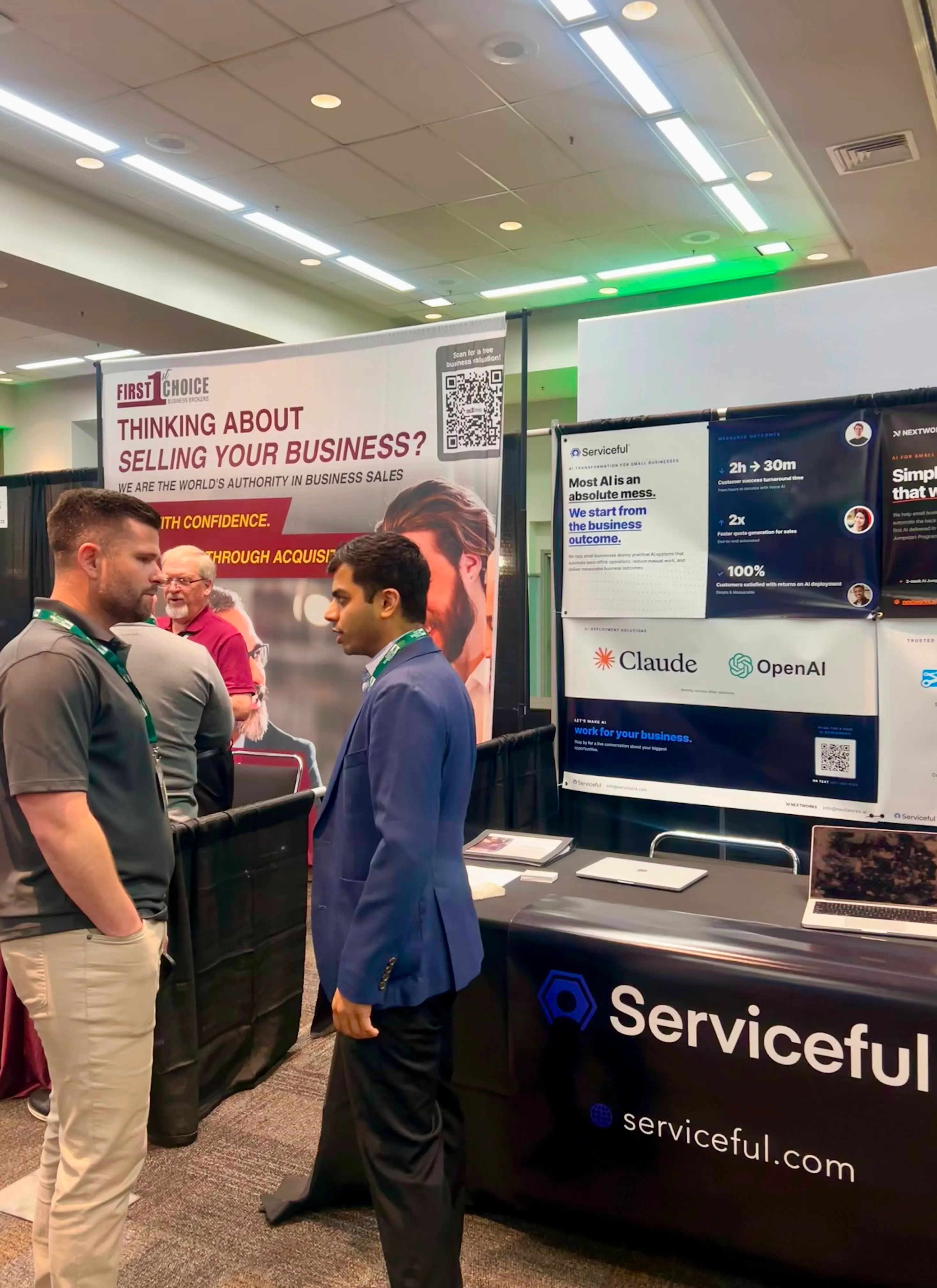 A Serviceful team member in conversation with an attendee at the booth, with Claude and OpenAI partner logos on the display behind