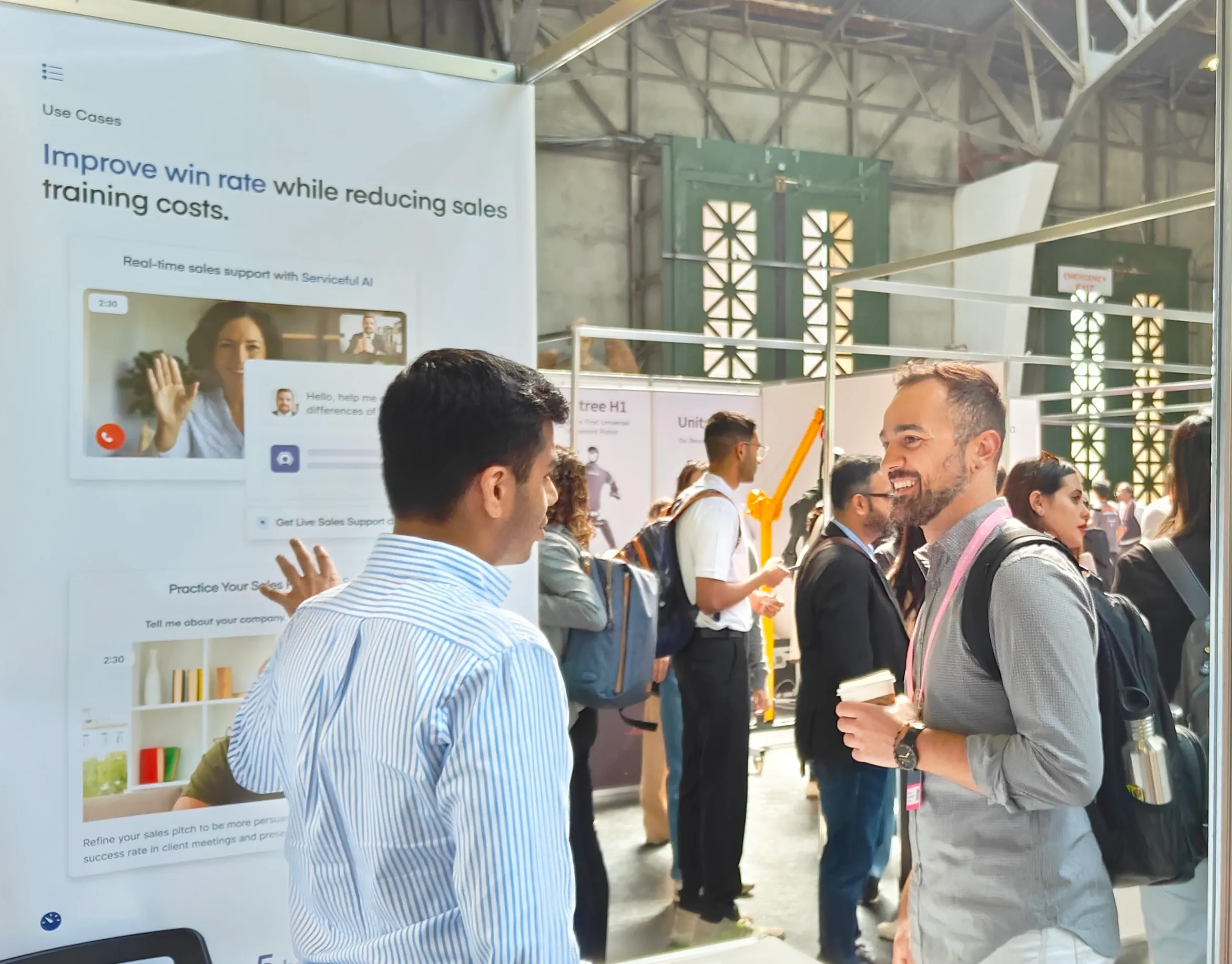 Two attendees in conversation beside a Serviceful banner reading "Improve win rate while reducing sales training costs"