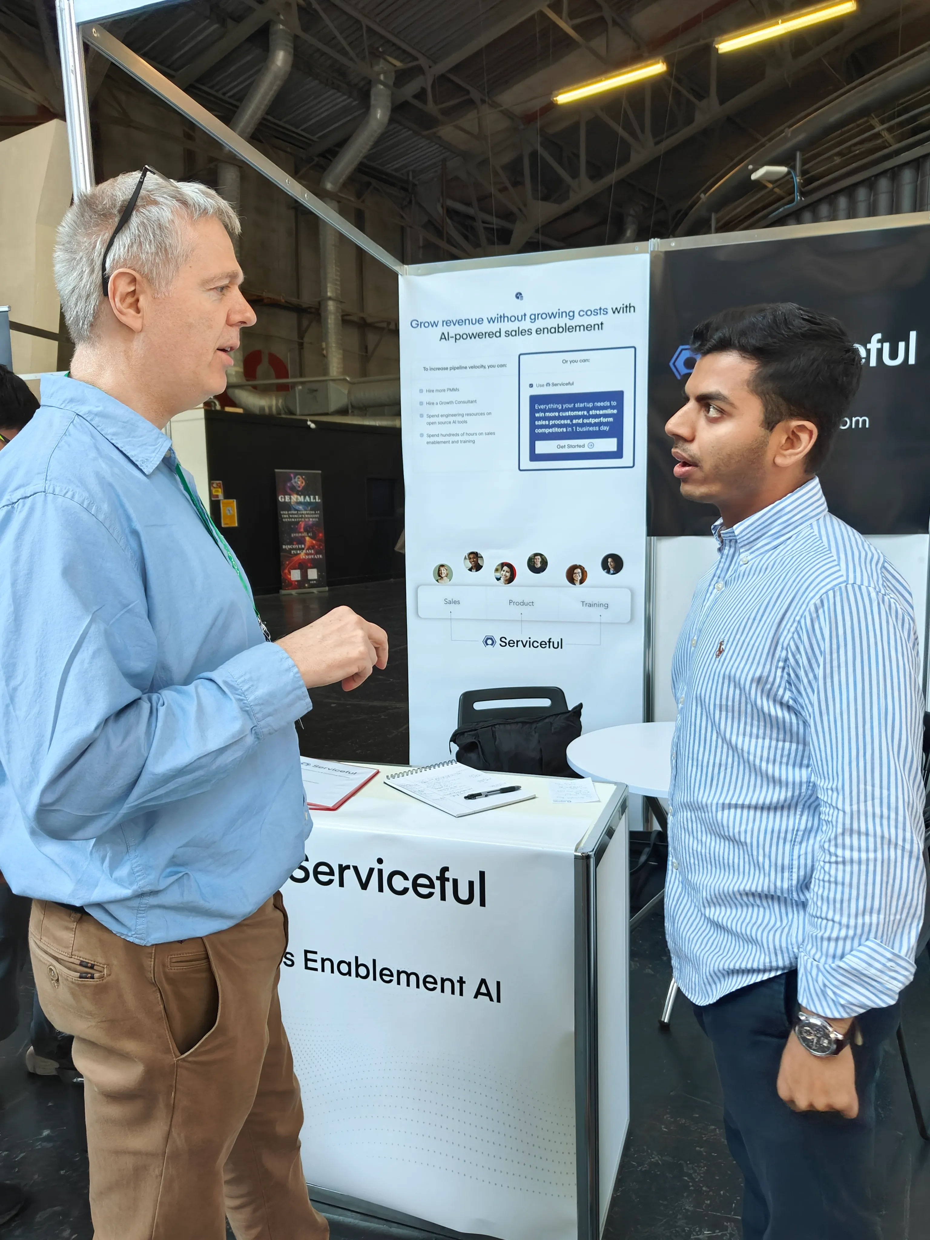 A Serviceful representative discussing AI-powered sales enablement with a visitor at the booth counter