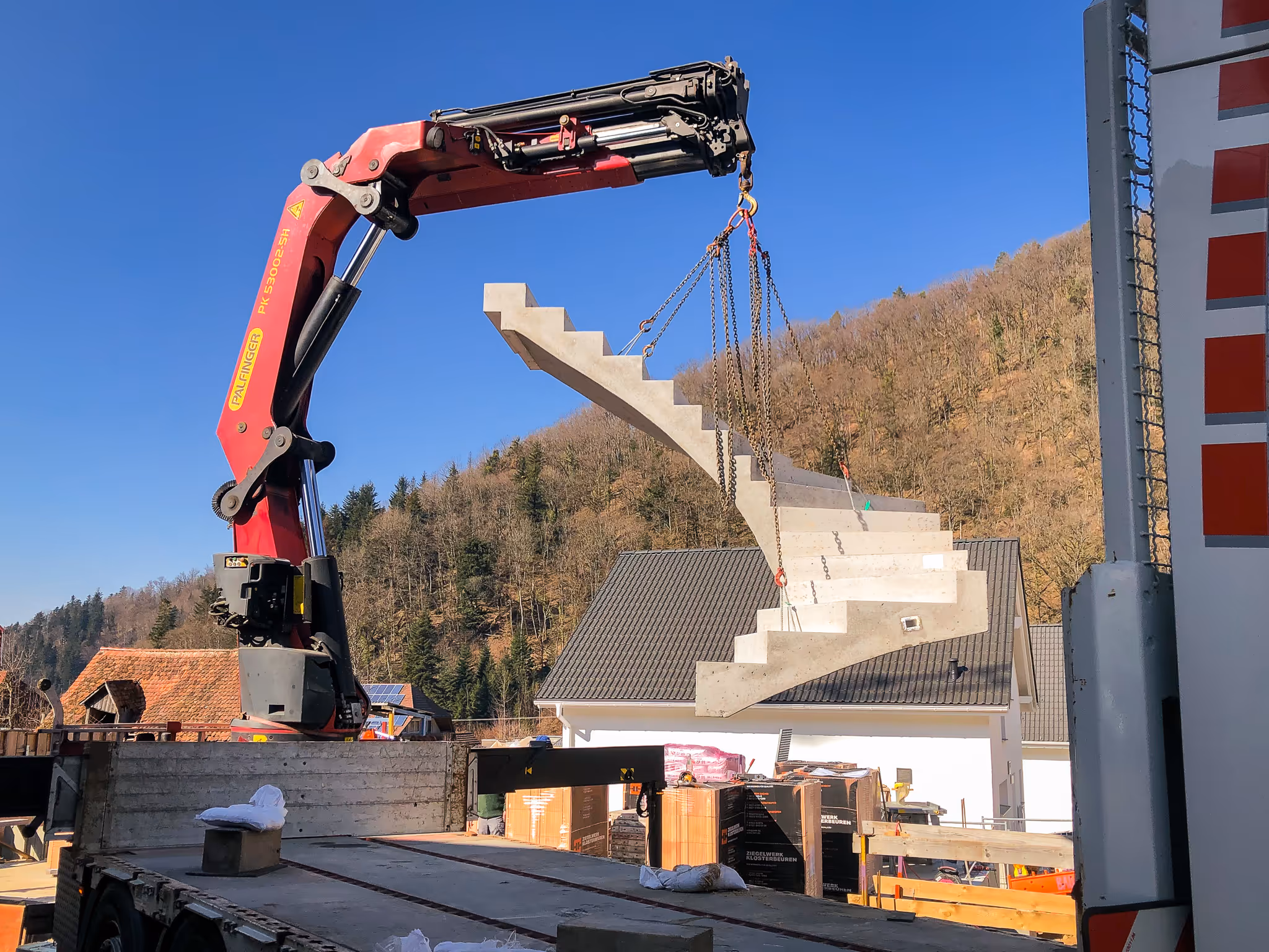 Kran hebt eine massive Fertigtreppe über ein Einfamilienhaus.