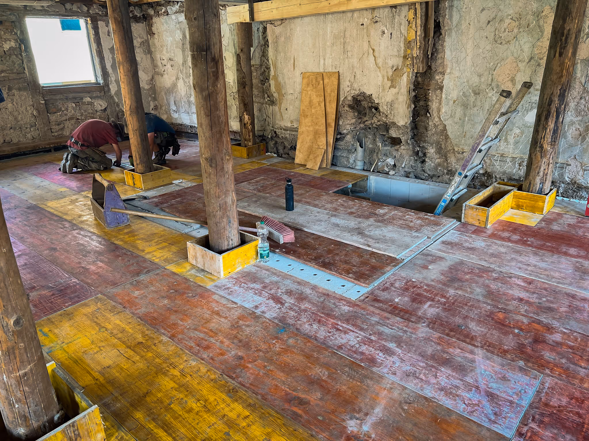 Innenraum mit alten Holzstützen und Schalungsplatten am Boden. Zwei Handwerker arbeiten an den Pfosten.