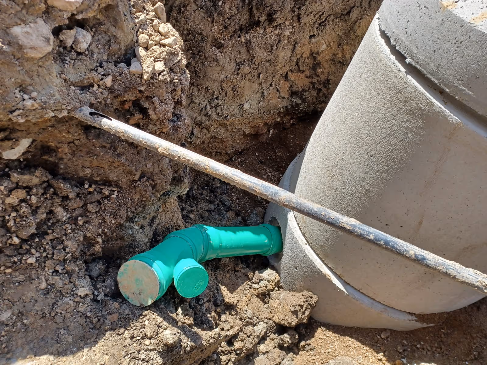 Grünes Abwasserrohr wird an einen runden Betonschacht in einer Baugrube angeschlossen.