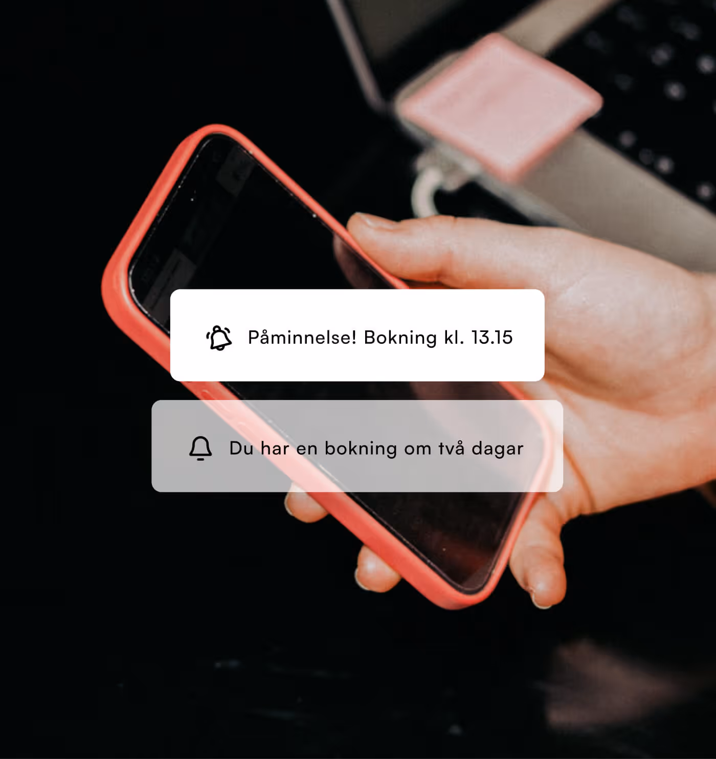 Hand håller en smartphone med röd kant, två notifikationer visas om bokningar: Påminnelse för bokning kl. 13.15 och en bokning om två dagar.