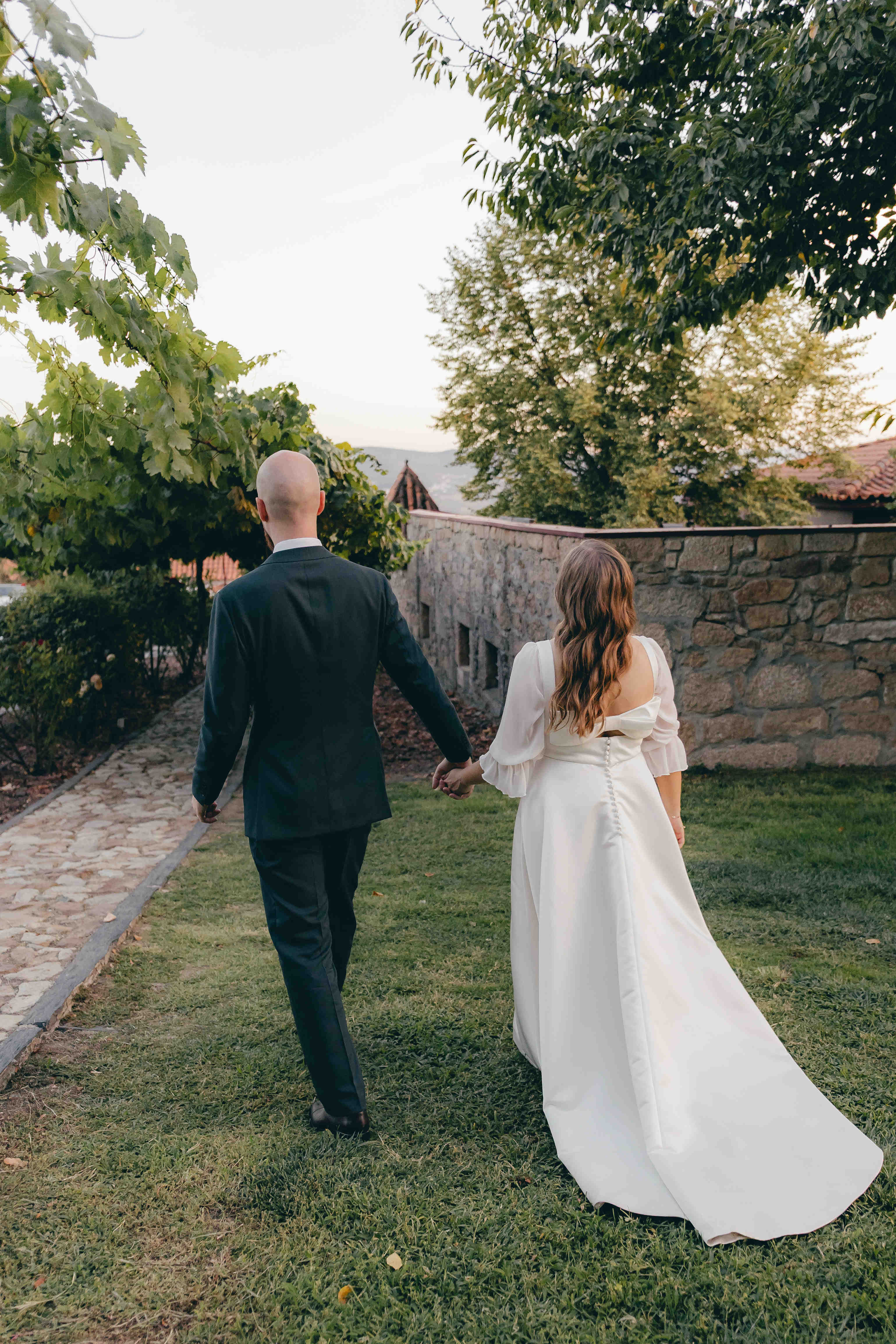 Melissa und Anders gehen Hand in Hand zurück durch den Garten; ihr Kleid bewegt sich hinter ihr.
