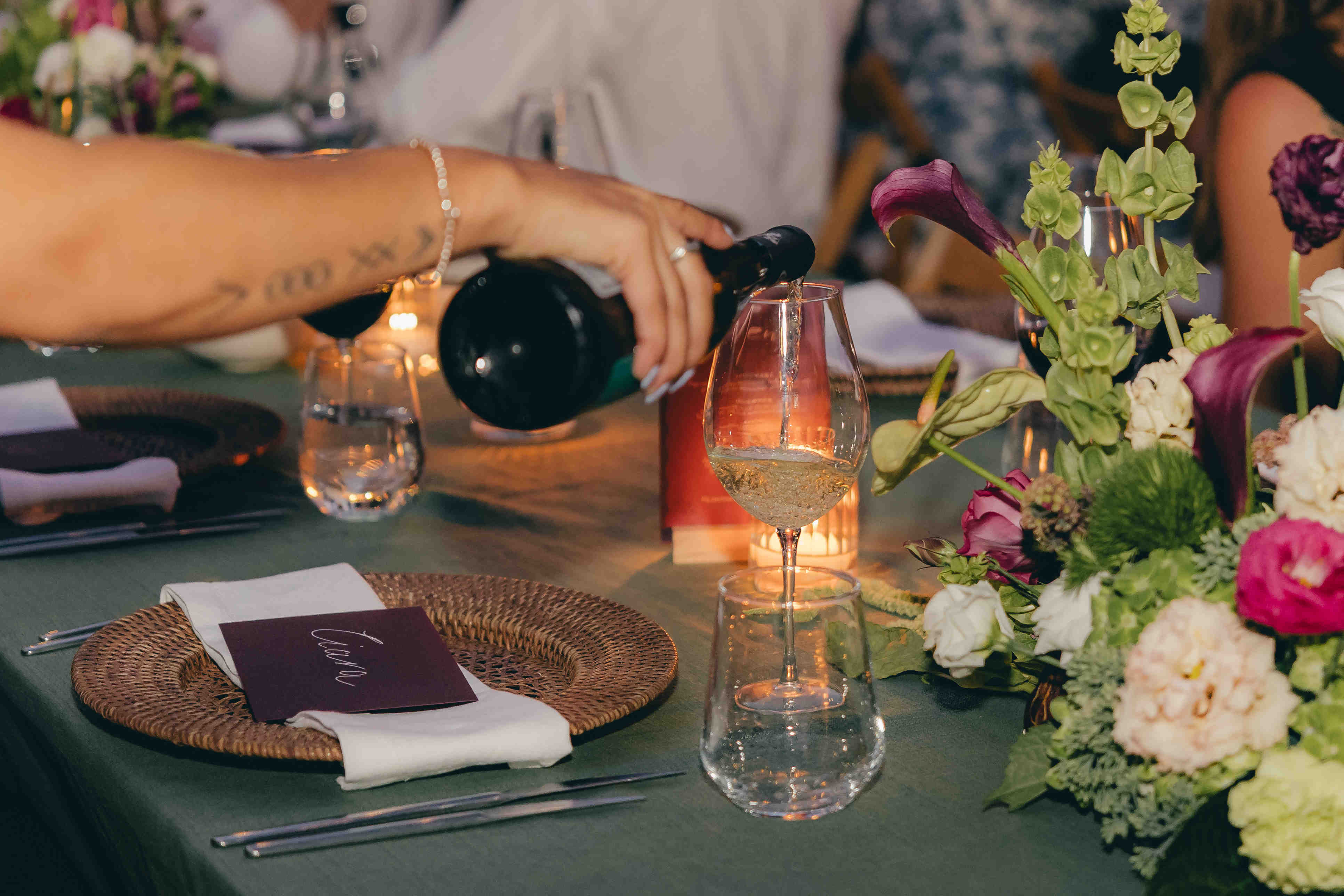 Wein wird zwischen Blumen und Kerzen in ein Glas an der Hochzeitstafel eingeschenkt.