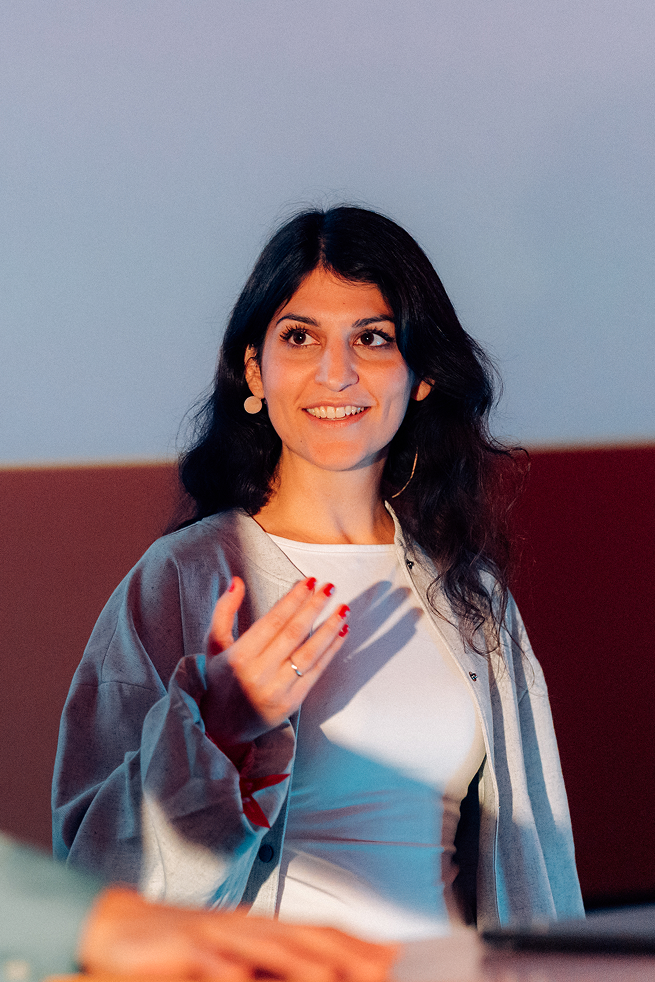 Zamina Ahmad mit langen dunklen Haaren spricht und gestikuliert während einer Präsentation.